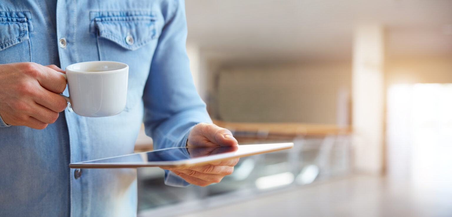 Close up of a male hands holding white digital tablet and cup of coffee